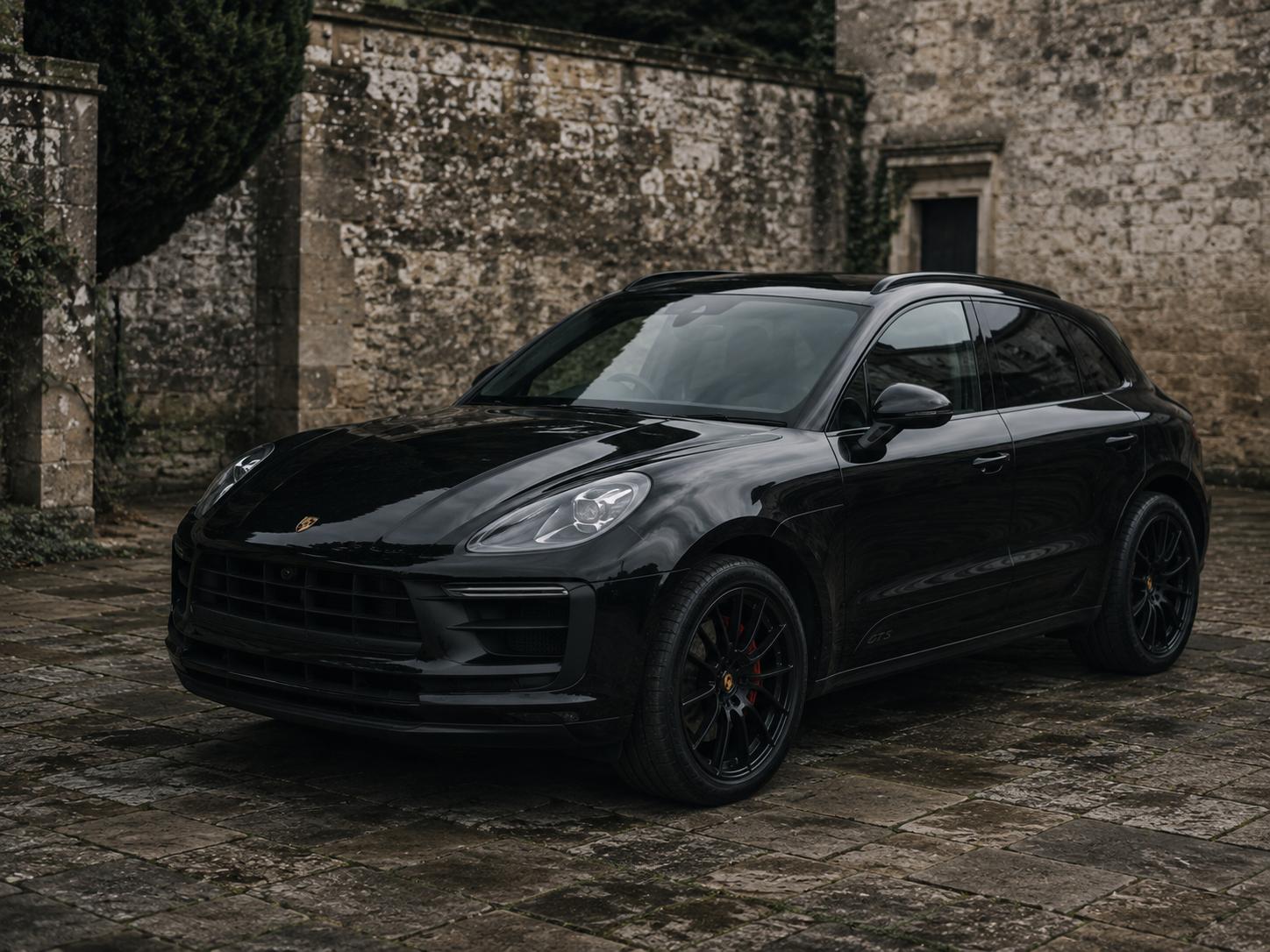 Black Porsche Macan GTS, three-quarter side profile, on a gravel drive.